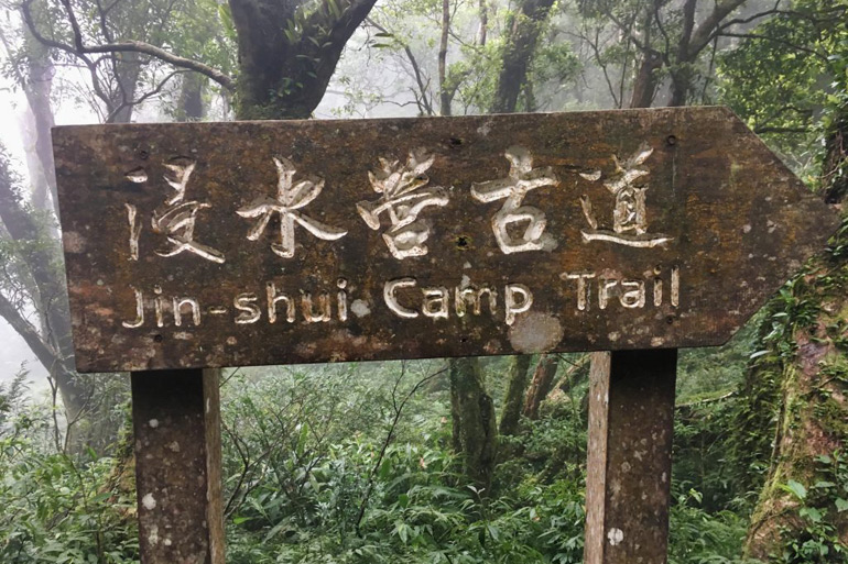 Wooden sign in forest that says "JinShui Camp Trail – 浸水營古道