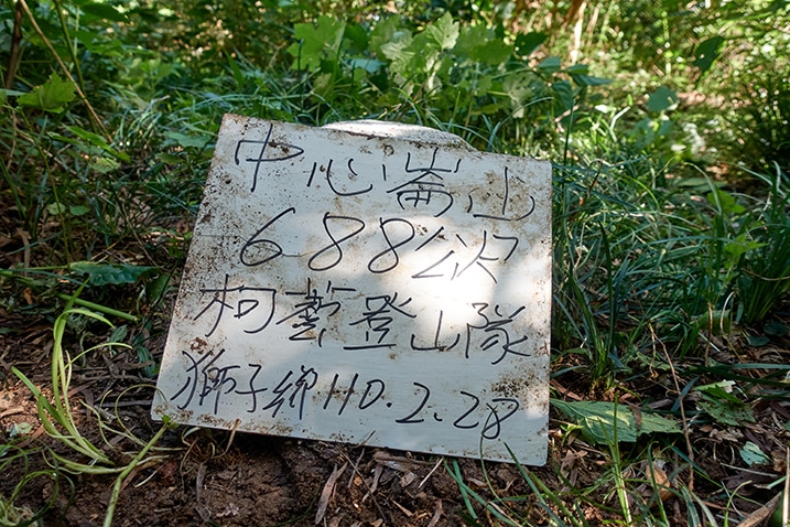 White sign leaning against triangulation stone - Chinese words on sign