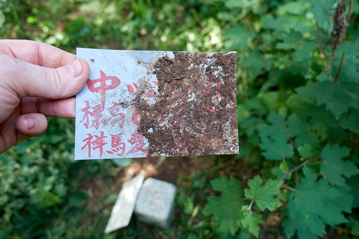 Hand holding small metal sign with Chinese words on it - half sign is dirty and unreadable 