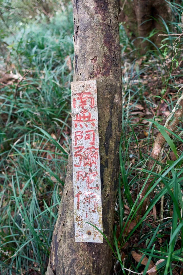 Metal sign attached to tree with Chinese writing on it