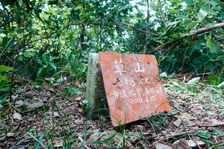 Red metal sign with Chinese writing on it leaning on triangulation stone for Caoshan - 草山