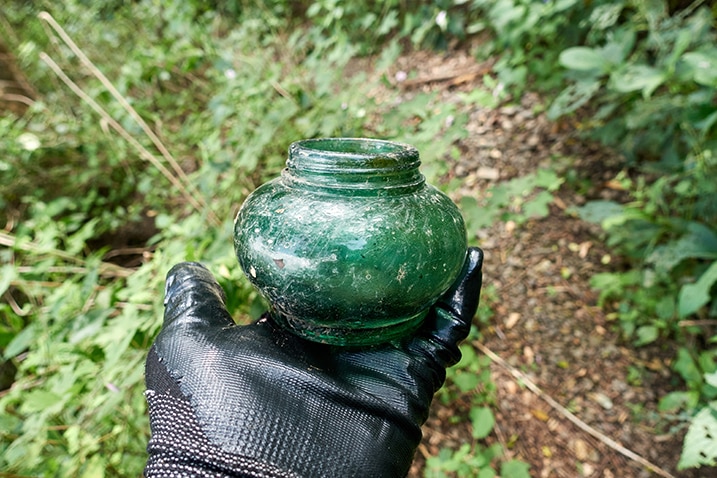 Black gloved hand holding a small dark green-ish container