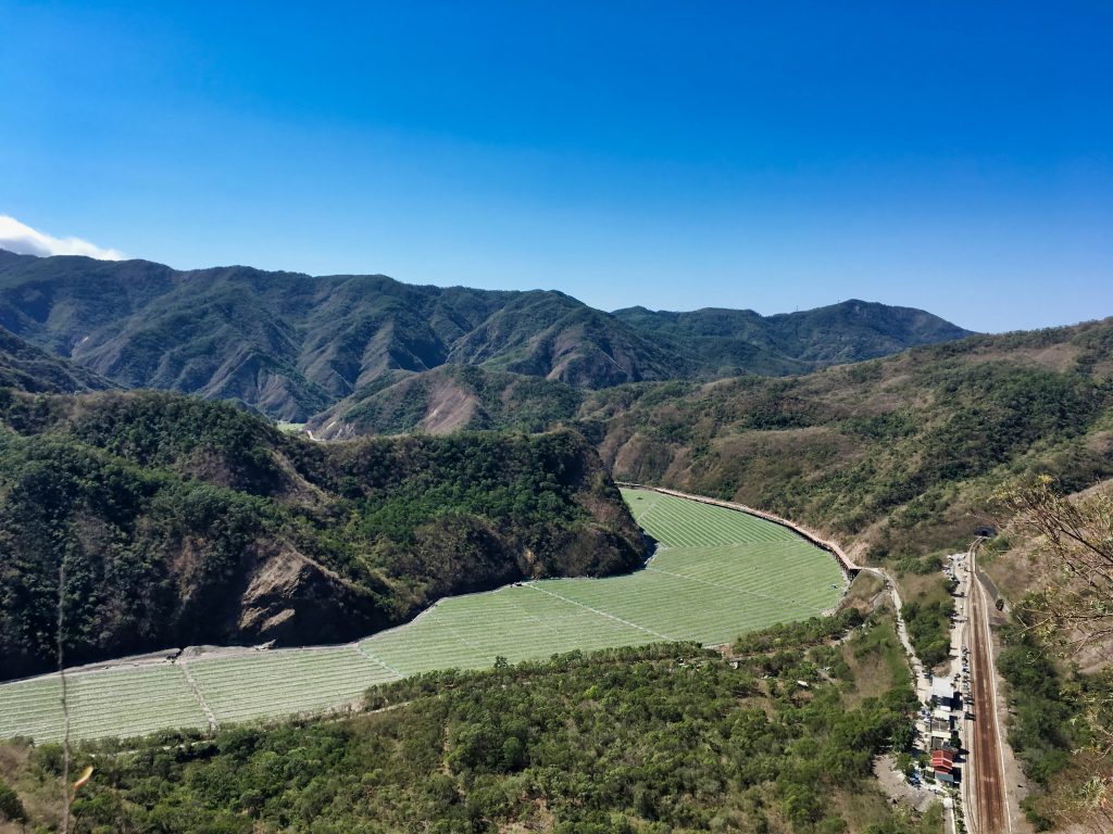 Looking down at watermelon fields planted in dry riverbed - blue sky and mountains - train relay station