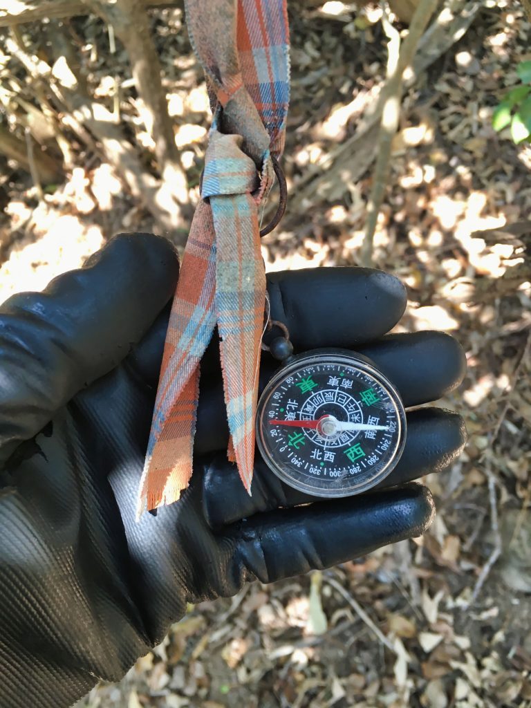 Gloved hand holding compass in Chinese attached to torn cloth