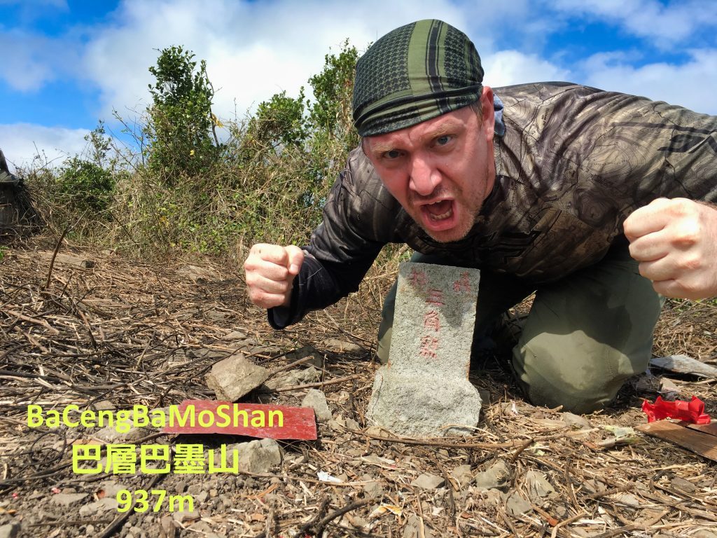 Man posing victoriously behind triangulation stone for 巴層巴墨山