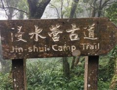 Wooden sign in forest that says "JinShui Camp Trail – 浸水營古道