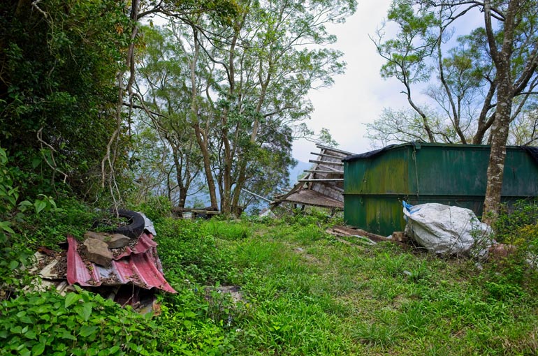 Grassy area with debris at side and large green container with destroyed structure behind