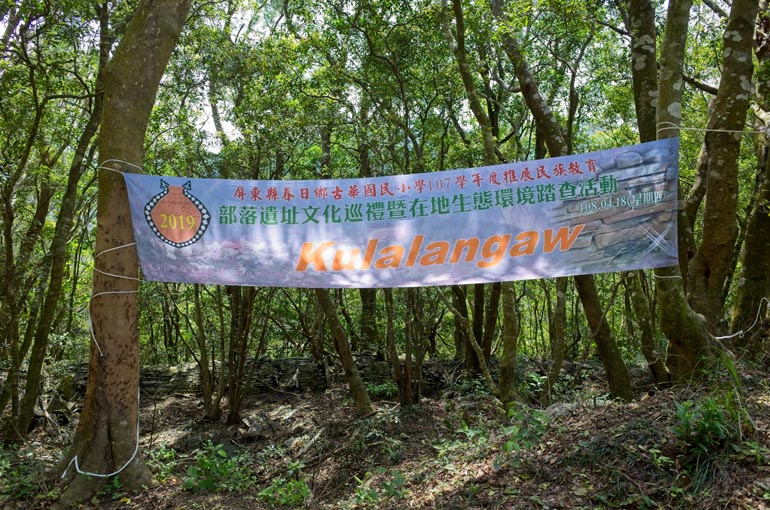 A banner strung from tree to tree with Chinese and Kulalangau written on it