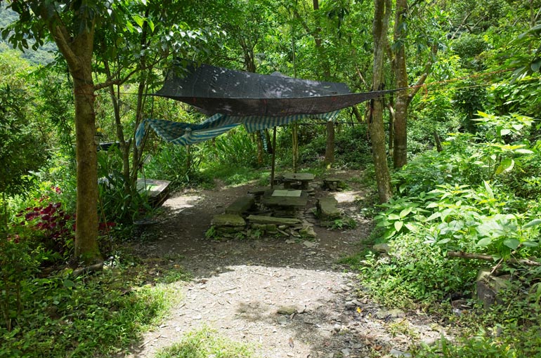 Cleared area with black tarp above and tables and benches made from stacked stones