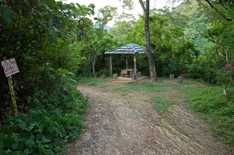 Dirt road passing a gazebo with stone chairs and a table