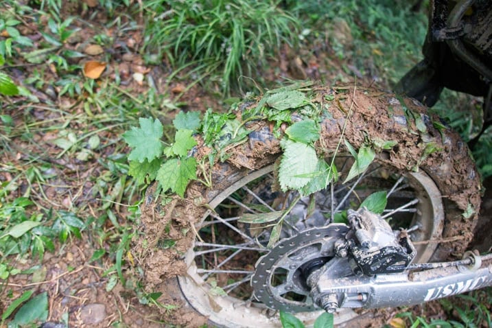 Closeup of motorcycle rear knobby tire filled with mud and leaves