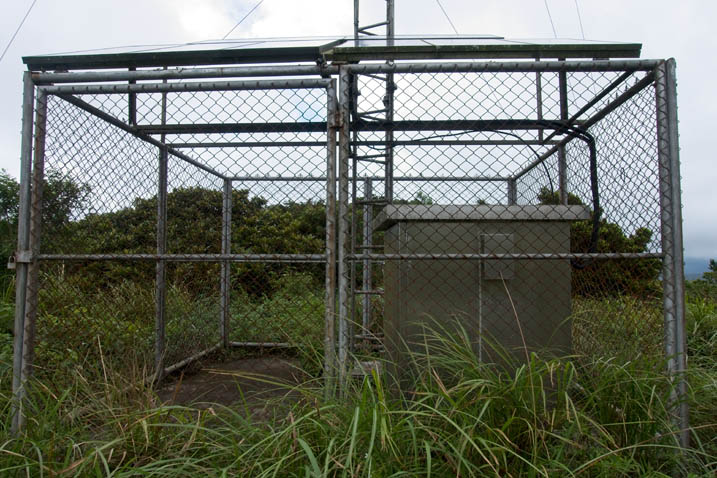 Base of antenna and large metal enclosure surrounded by a fence