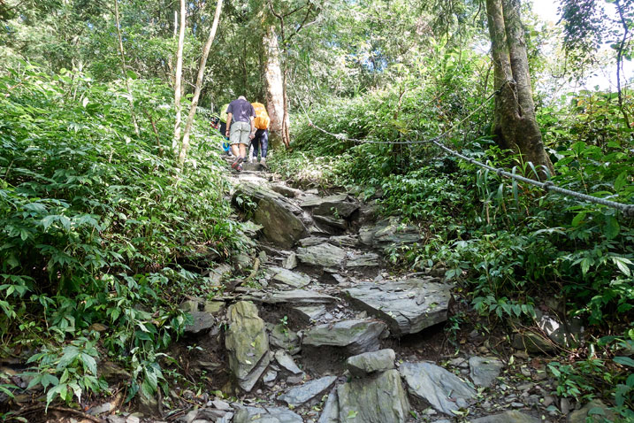 Wide rocky trail - rope on one side and hikers at top