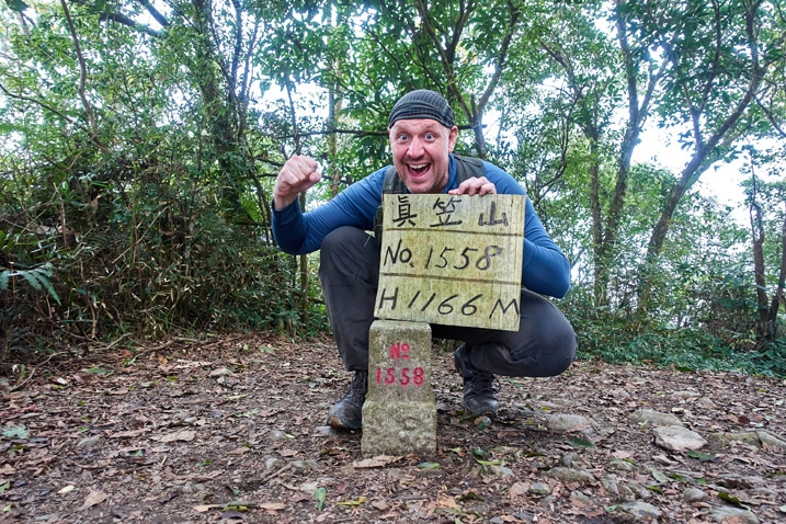Man standing behind triangulation stone holding a sign