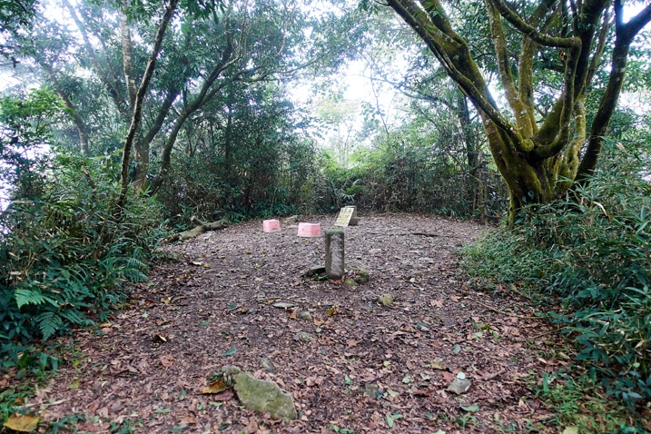 Mountain peak - open area with two stone markers and plastic stools - trees all around