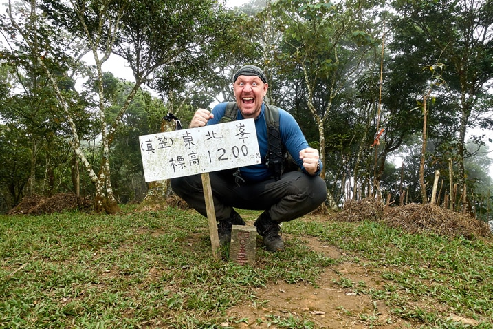 Man with triumphant pose behind a triangulation stone - holding sign