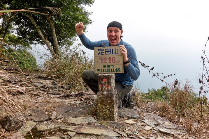 Man posing behind ZuMuShan 足母山 triangulation stone in triumphant pose
