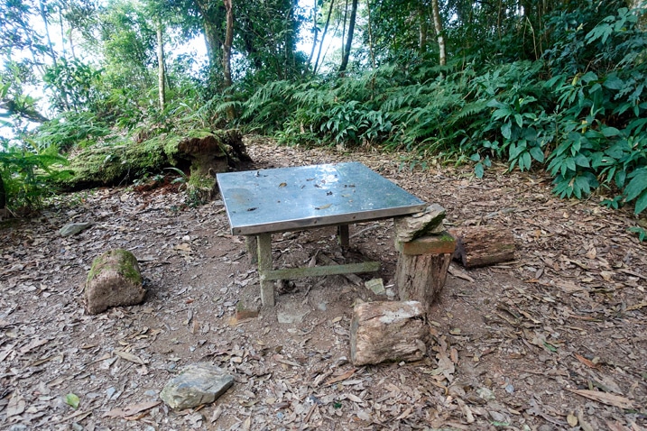 A metal table in the middle of an open area - trees in the background - WeiLiaoShan 尾寮山 trail