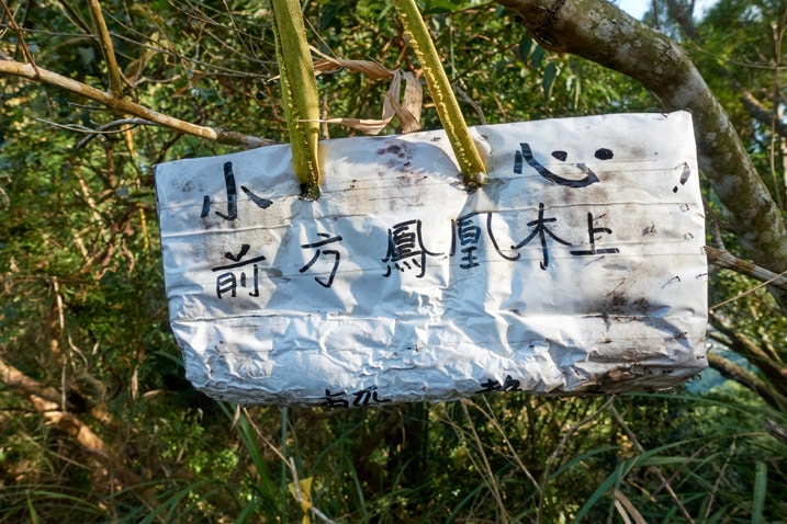 White sign with Chinese hanging from tree - 旗月縱走