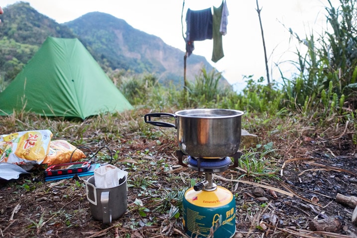 Water boiling on camp stove - tent, clothes hanging, and mountain in background