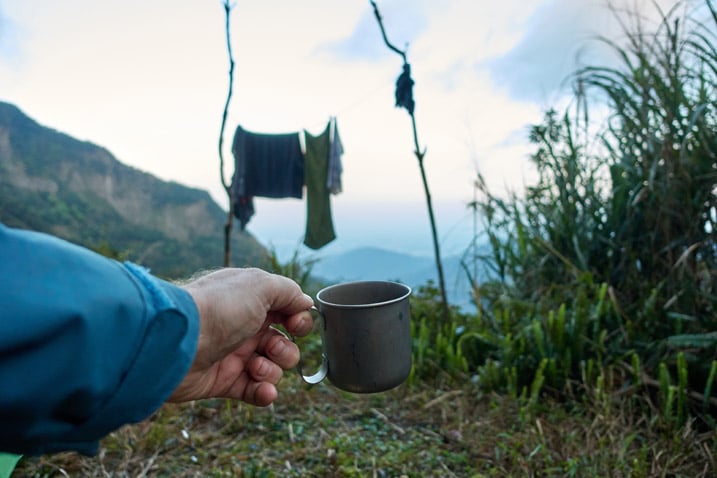 Hand holding titanium coffee cup - clothes hanging in background - mountains in distance