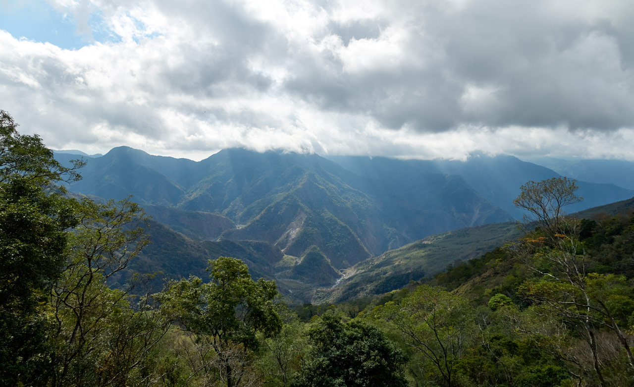 Looking down at mountains and riverbed - sunbeams shooting down from cloudy sky