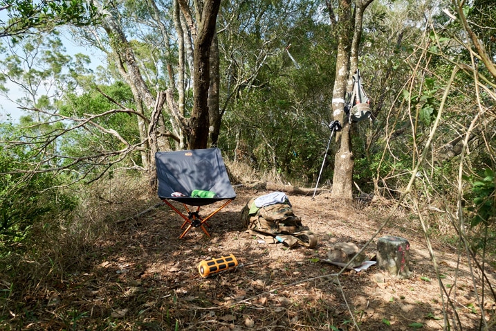 Camp chair, backpack and misc items on ground on mountain peak - trees all around