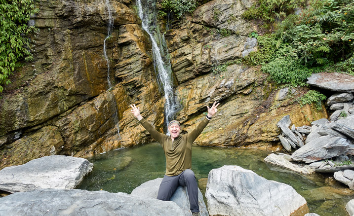 Man in front of waterfall with arms stretched out