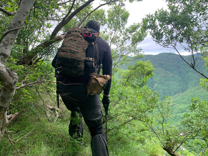 Man with camouflage backpack walking out to edge of rock peak
