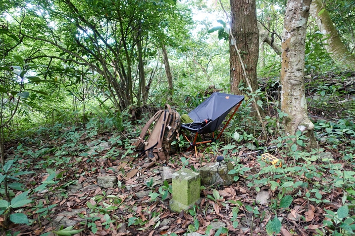 Camp chair and backpack set up near a triangulation stone - trees in background