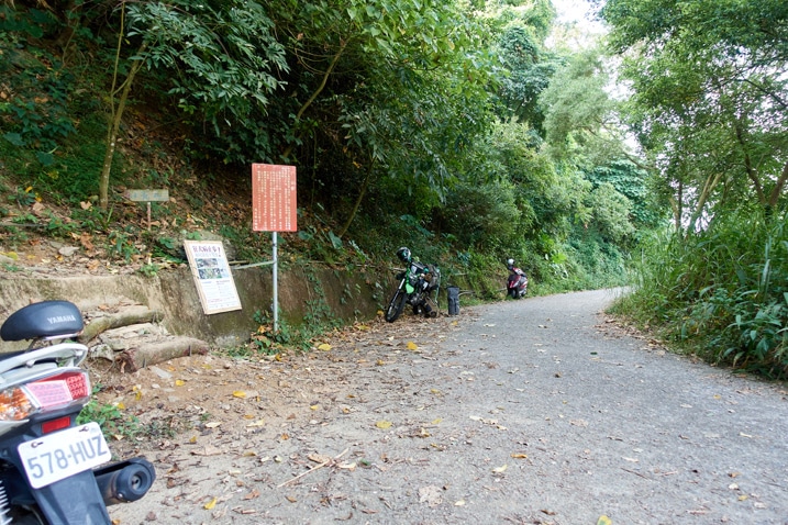 Mountain road with motorcycles parked - signs on left