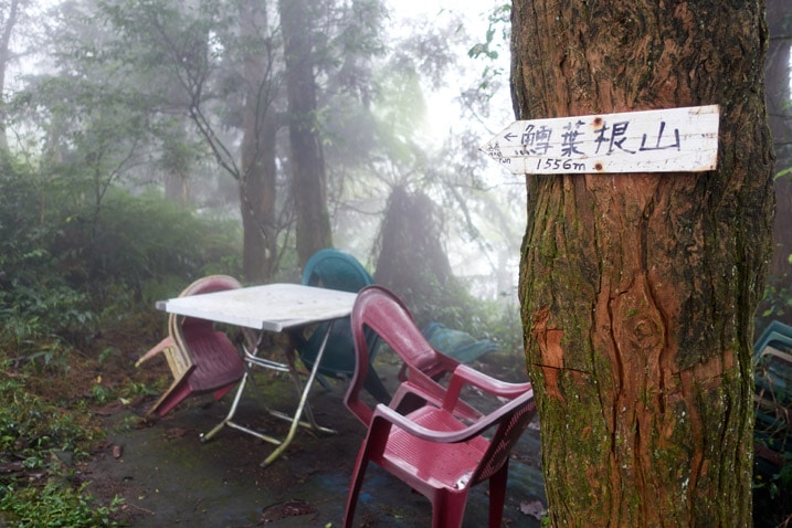 Table and plastic chairs on mountain ridge - tree with sign pointing to the left