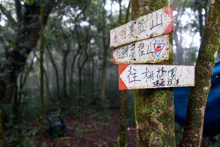 Three signs in Chinese pointing the directions to different mountains - trees in background