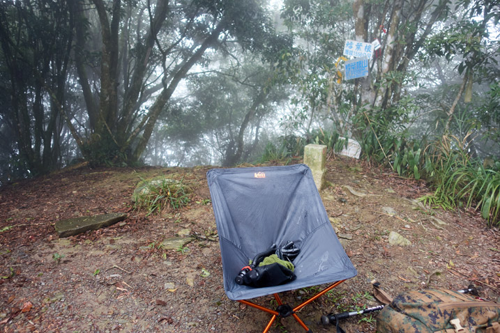 Camp chair on mountain peak - open area - trees in background - foggy