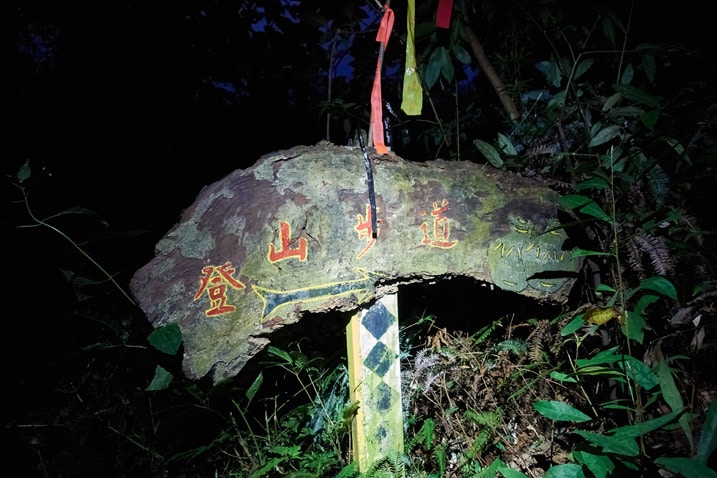 Wooden sign in the dark lit up by headlamp - Chinese words written on sign