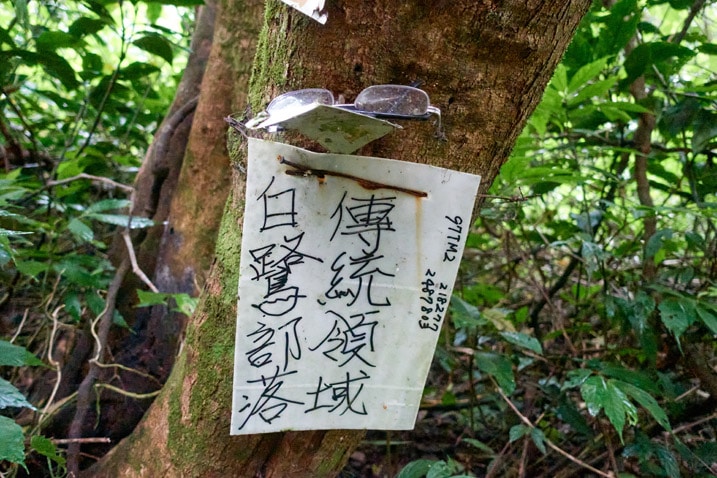 White sign attached to tree with black Chinese writing on it - lost glasses at top of sign