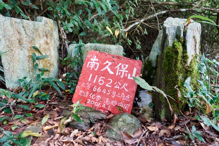 Red sign with white chinese letters leaning against a stone for NanJiuBaoShan 南久保山