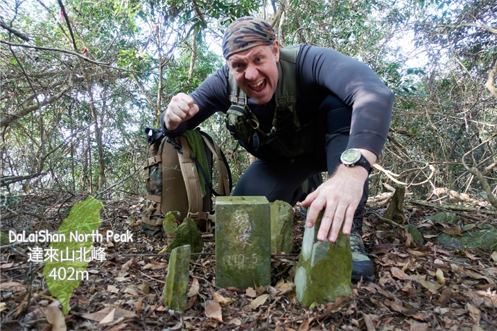 Man kneeling behind stone peak marker in triumphant pose