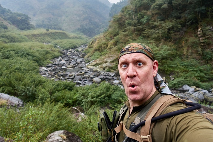 Man taking a selfie with small, rocky riverbed behind him