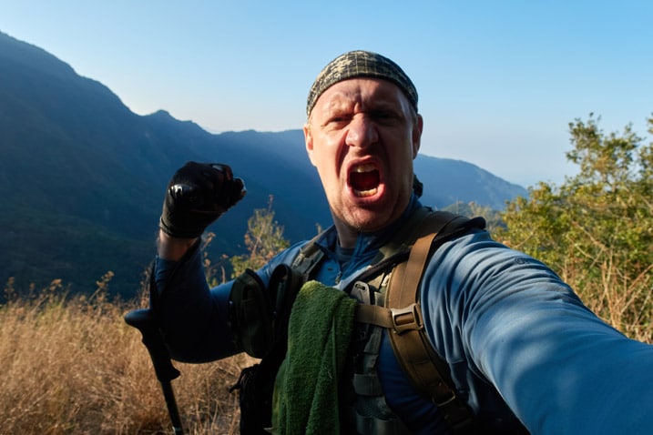 Man yelling triumphantly for some reason - hand in fist - mountains and blue sky in background