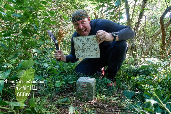 Man kneeling triumphantly behind triangulation stone of ZhongXinLunSheShan 中心崙社山