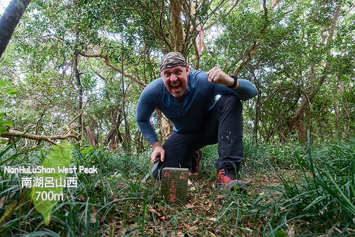 Man kneeling triumphantly next to triangulation stone of NanHuLuShan West Peak - 南湖呂山西