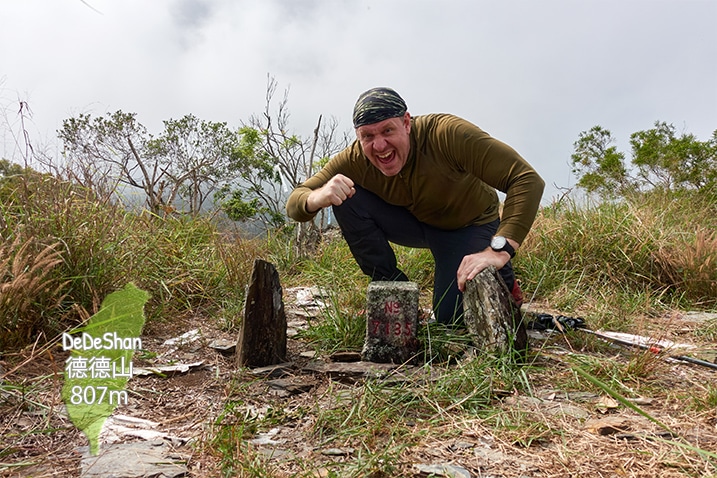 Man kneeling triumphantly behind a triangulation stone on a mountaintop